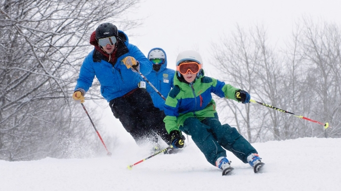 A vibrant winter sports scene at Mont Habitant Quebec featuring a skier and a family enjoying skiing against the majestic backdrop of the winter sports centre.