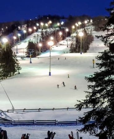 Winter scene at Mont Habitant in Quebec, Canada, featuring a bustling ski resort with patrons enjoying snow sports, a running ski lift, and a quaint chalet visible in the distance.
