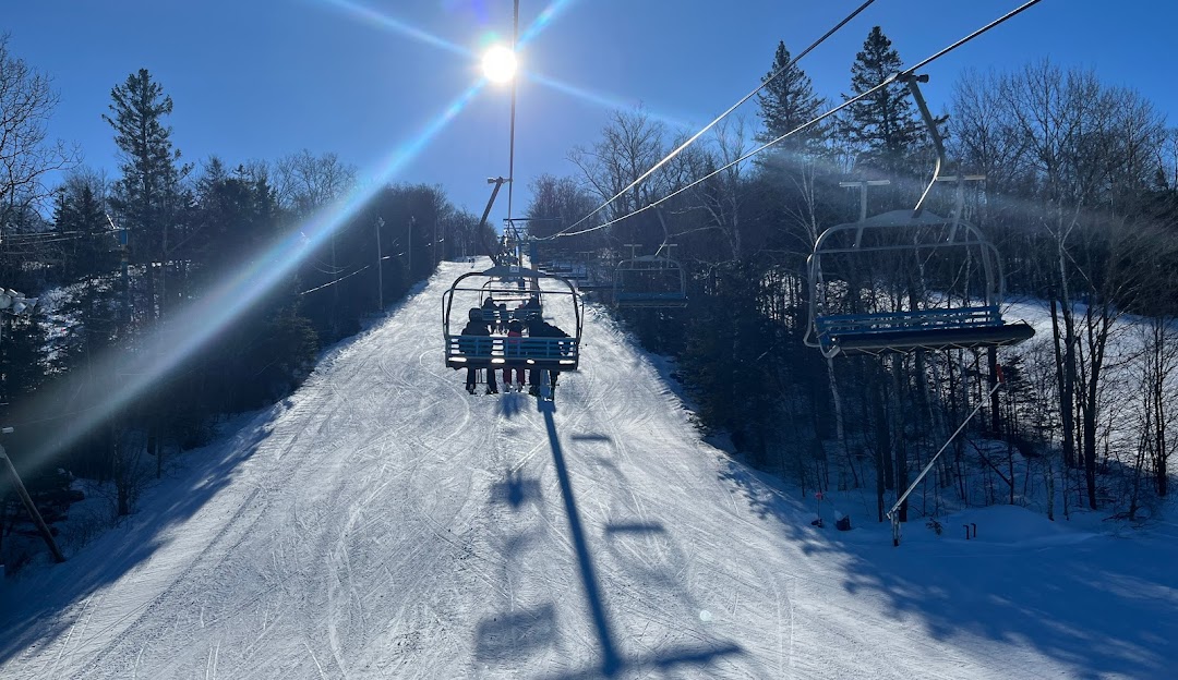 Ski lift rising above a lively winter sports scene at Mont Habitant ski resort, Saint-Sauveur, Quebec. Skiers enjoying a sunny day on the slopes.