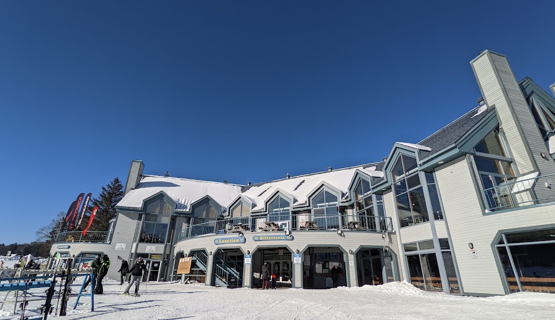 View of Mont Habitant ski resort in Laurentides, displaying a winter sports centre and scenic snowy landscape. A challet is seen in the foreground, offering a quintessential Quebec experience.