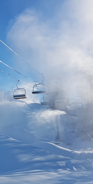 Ski lift moving amidst the snow-capped scenery of Mont Habitant, a popular ski resort in Quebec. Skiers navigate the slopes below while a charming chalet waits in the distance.