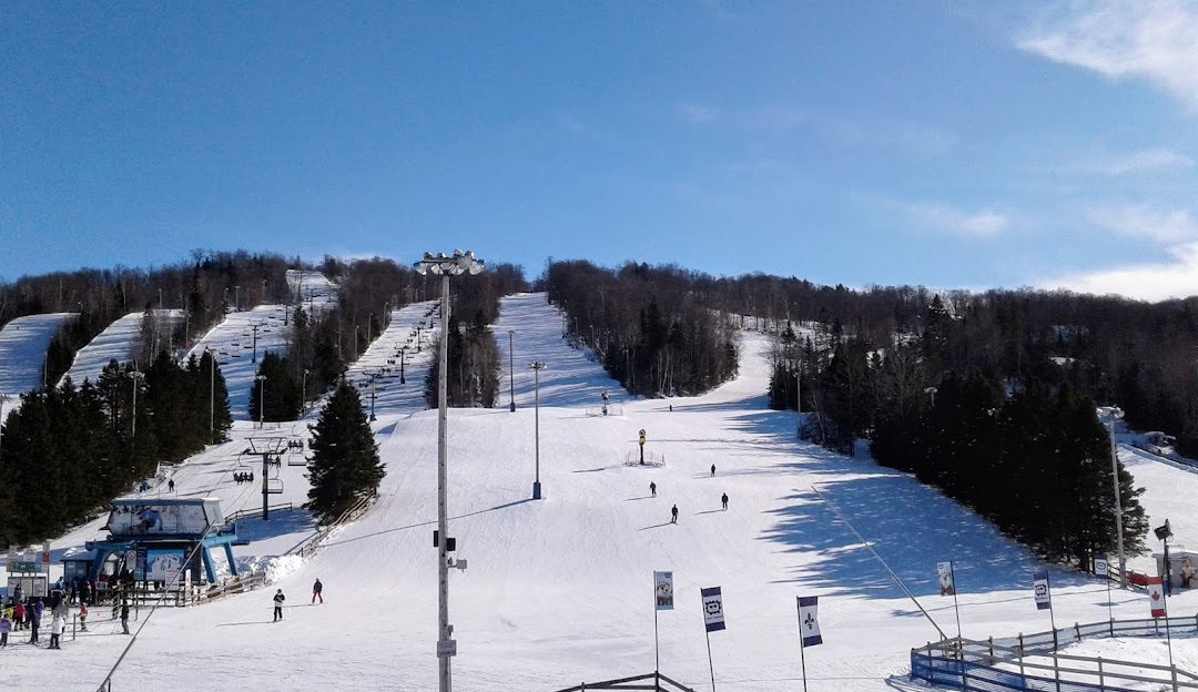 Winter image of Mont Habitant ski resort in Quebec, Canada, depicting a bustling scene of winter sports, a ski lift in operation, and snow-covered slopes. A charming challet is also visible.