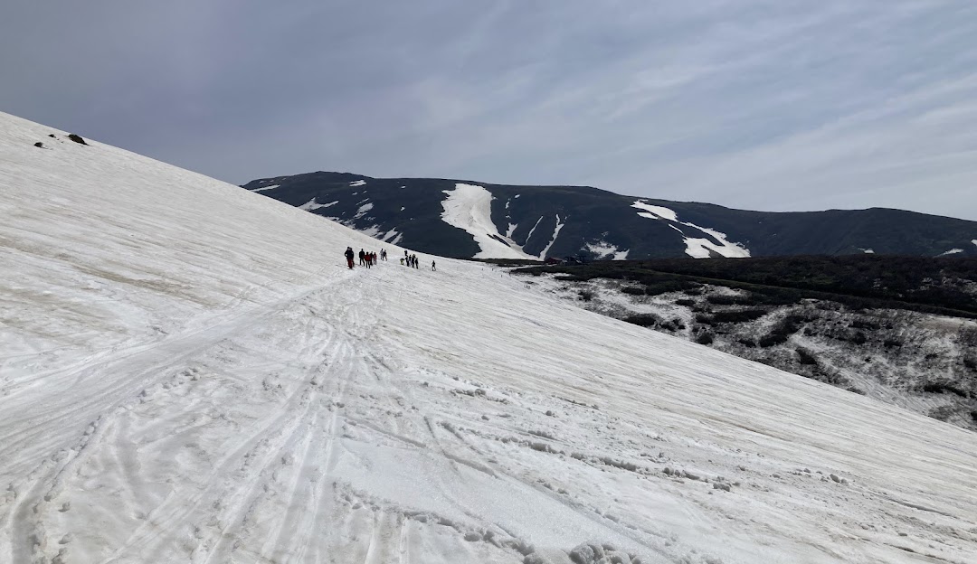 Winter scene at Gassan Ski Resort in Tōhoku, Japan with skiers enjoying the slopes, a chalet nestled amongst the wintry landscape, and a majestic mountain in the background.
