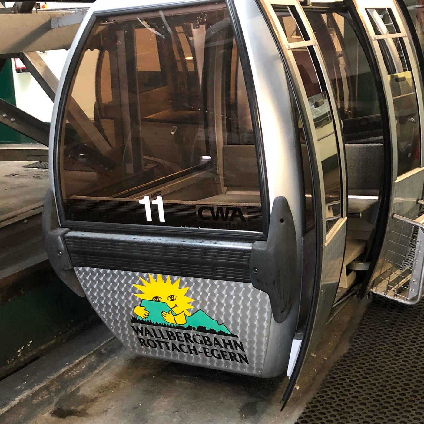 A sunny day at a ski resort in Wallberg, Germany, highlighting a ski lift alongside a quaint chalet. A snowmobile can be spotted near the facilities, all nestled amid a snowy backdrop.