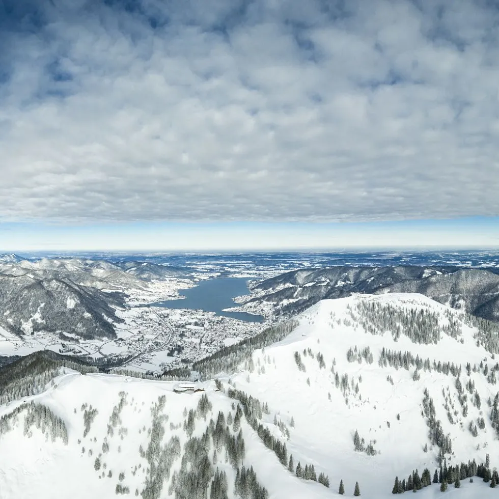 Winter sports enthusiasts enjoying a day at the Wallberg ski resort in Upper Bavaria, Germany. The image showcases snow-covered slopes against a backdrop of beautiful, majestic mountains.
