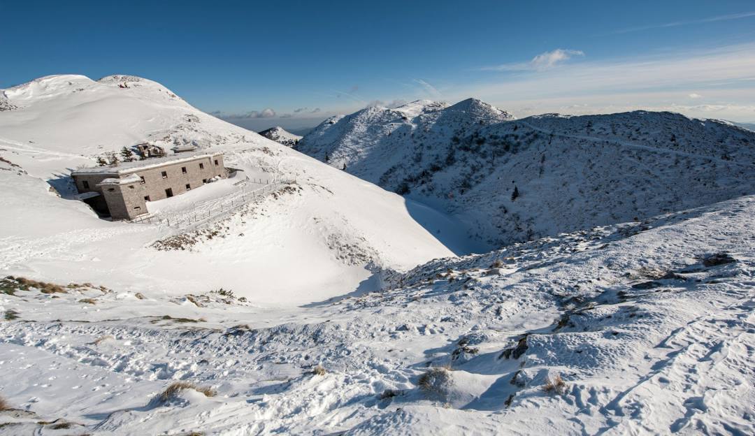 A picturesque view of Soriška Planina in Slovenia featuring a winter sports centre and a ski resort nestled amidst a beautiful mountain landscape. A charming challet is also visible in this winter sports scene.