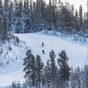 A skier and a snowmobile are captured in a winter sports scene at Tännäskröket in Northern Sweden. A small group of people are skiing in the background at this popular ski resort.