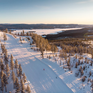 Winter scene at Tännäskröket ski resort in Northern Sweden, featuring a skier in action. The landscape filled with snow and a ski lift is partial visible.