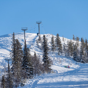 A ski lift ascends a snow-covered slope at Tännäskröket ski resort in Northern Sweden. A skier enjoys winter sports against the backdrop of picturesque Funäsfjällen mountains.