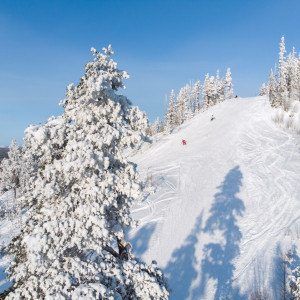 Winter sports enthusiasts enjoy a day at the Tännäskröket ski resort in Jämtland, Northern Sweden. A skier descends a slope while a snowmobile trails in the background, all against the backdrop of a serene, snow-covered landscape.