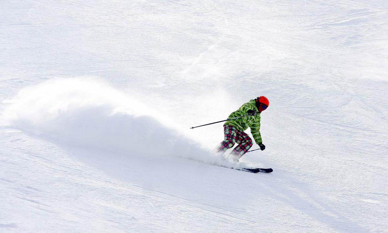 A skier gracefully glides down a snowy slope in Orlovka Kyrgyzstan. The background showcases the charming architecture of a chalet in this popular ski resort. The energy of winter sports is palpable.