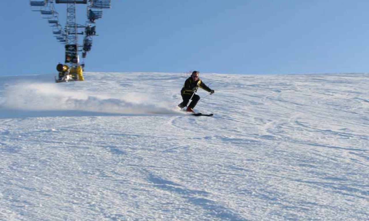 A skier is enjoying a winter day on the slopes in Orlovka Kyrgyzstan. The nearby chalet and ski lift indicate that this is a bustling ski resort. The scene is a representation of vibrant winter sports activity.