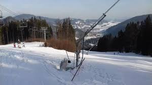 A ski lift at Ski Park Racibor in Oravský Podzámok, Žilina, Slovakia surrounded by alpine trees with a snow-covered chalet in the background, depicting a typical winter sports scene.