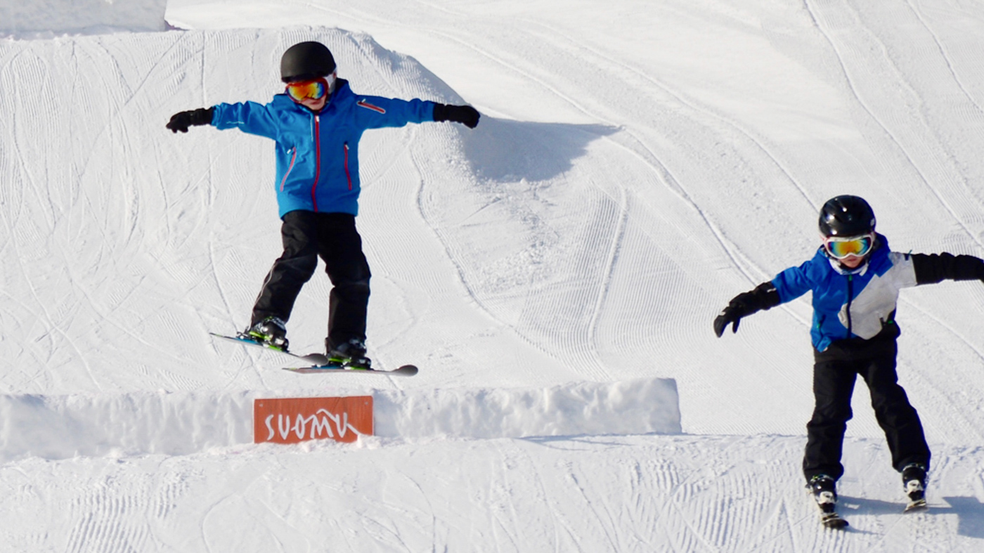 A snowboarder navigating the snowy slopes of Suomutunturi in Lapland, Northern Finland, leaving a trail of kicked-up snow against a stark winter backdrop.