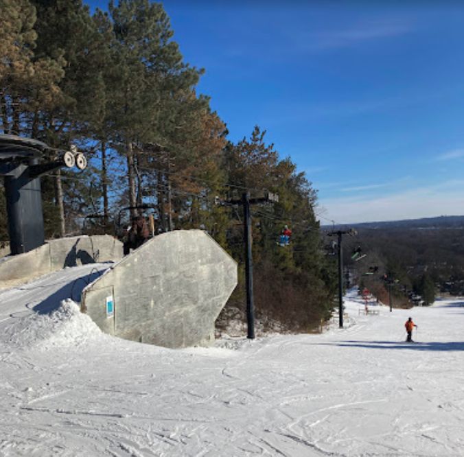 Winter scene at Alpine Valley in White Lake, Michigan, showcasing a bustling ski resort with active skiers navigating the snow-covered slopes, and ski lifts transporting more enthusiasts to the mountain top.