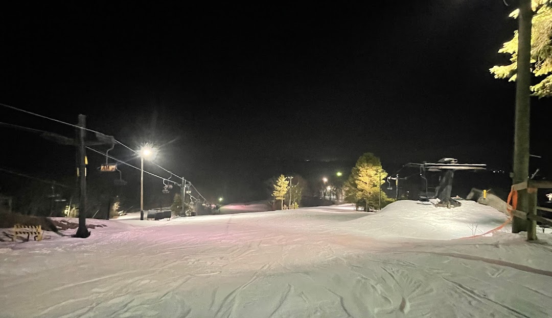 An appealing winter scene at Alpine Valley Ski Resort in White Lake, Michigan. Skiers glide down the snowy slope dotted with trees, while others ascend the mountain on a ski lift.