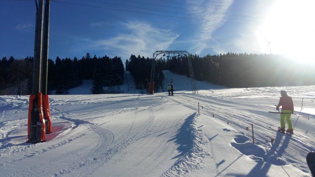 A winter sports scene in Tramelan Switzerland featuring a skier on a snow-covered slope with a charming chalet and winter sports centre in the backdrop.