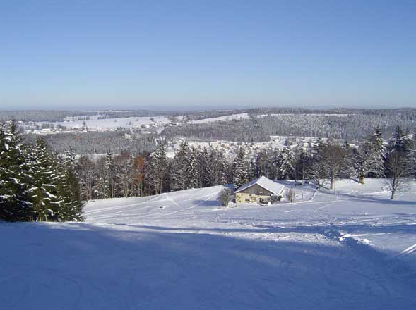 Winter sports scene at Tramelan Switzerland showcasing a charming chalet amidst a snow-filled landscape. The bustling winter sports centre can be seen completing the scenic view of the ski resort.