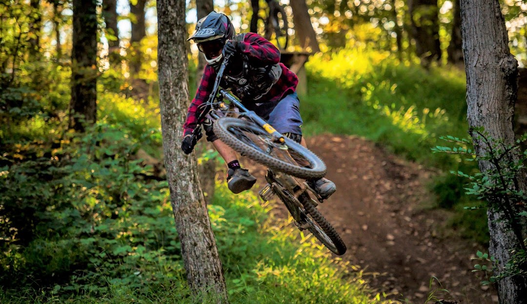 A person mountain biking at Powder Ridge Mountain Park & Resort in Middlefield Connecticut on a sunny day. A chalet is visible in the background.