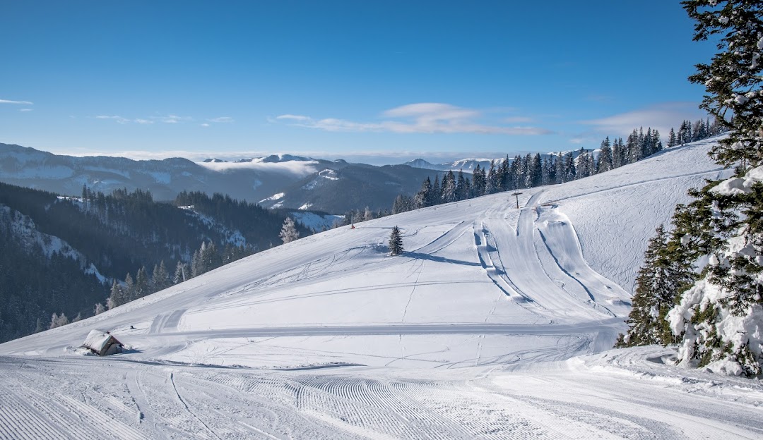 Ski scene in Niederalpl, Hochsteiermark, Austria showing a skier going down a snow-covered slope near a ski lift in a bustling winter sports location at a ski resort.
