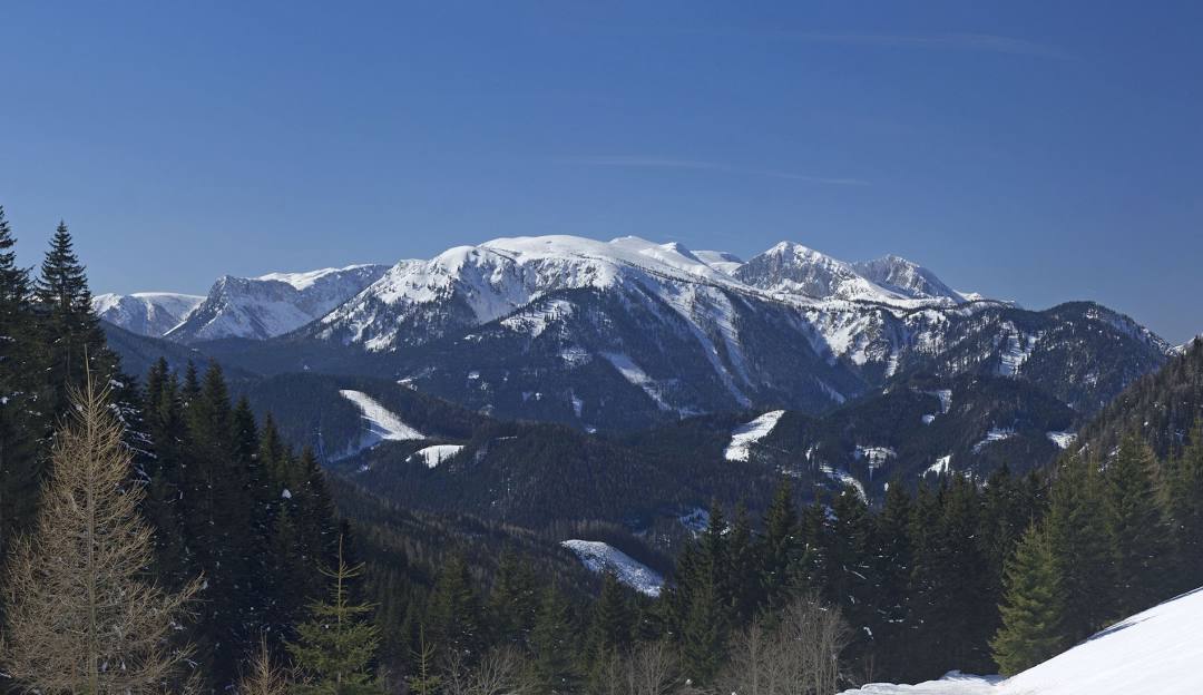 A picturesque winter scene in Niederalpl Austria featuring a quaint challet nestled amidst snowy mountains with skiers enjoying the nearby ski resort.