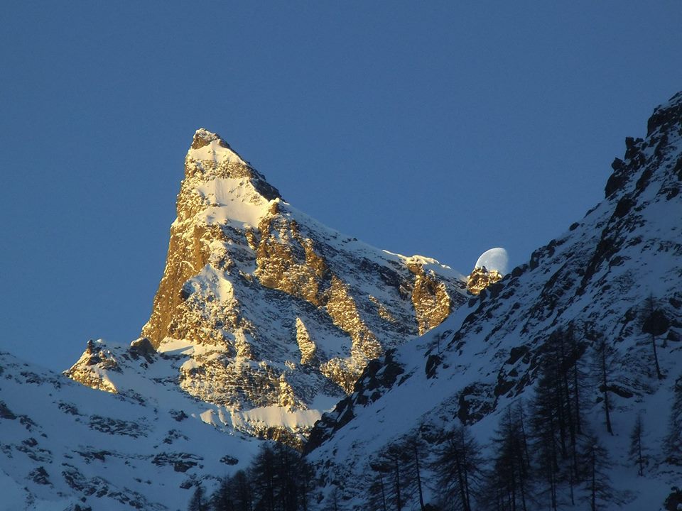 View of the charming Italian ski region, Rhêmes-Notre-Dame in Gran Paradiso, featuring a large, snow-covered mountain peak in the background and a cozy chalet and mountain hut amidst a winter sports scene.