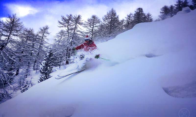 A skier and a snowboarder are enjoying the slopes at Rhêmes-Notre-Dame ski resort in Italy with a quaint chalet nestled amongst the snowy landscape in the background.