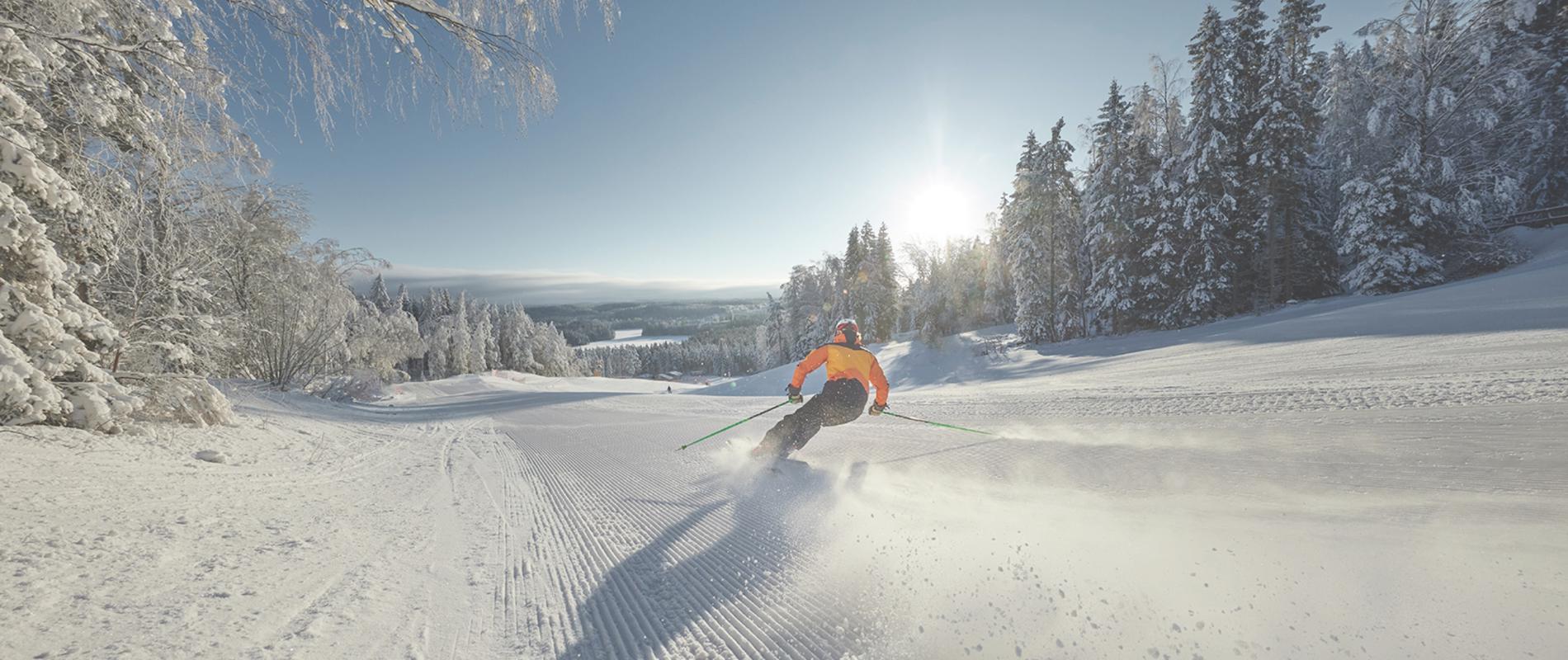 Winter sports scene captured at Isaberg Mountain Resort in South Sweden, with a skier and snowboarder in action amidst the backdrop of the ski resort and sports centre.