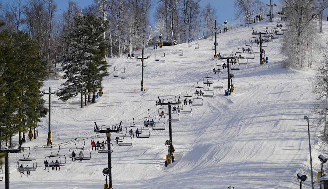Winter sports enthusiasts enjoying a day at Mad River Mountain ski resort in Zanesfield, Ohio. The ski lift is busy with skiers and snowboarders heading up the snow-covered slopes amidst stunning winter scenery.