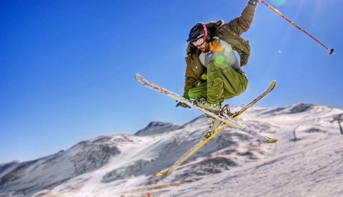 A skier in action at Mratkino in Beloretsk, Russia, with a distant view of a snowboarder and a ski lift. A chalet is also visible in the winter sports scene filled with snow.
