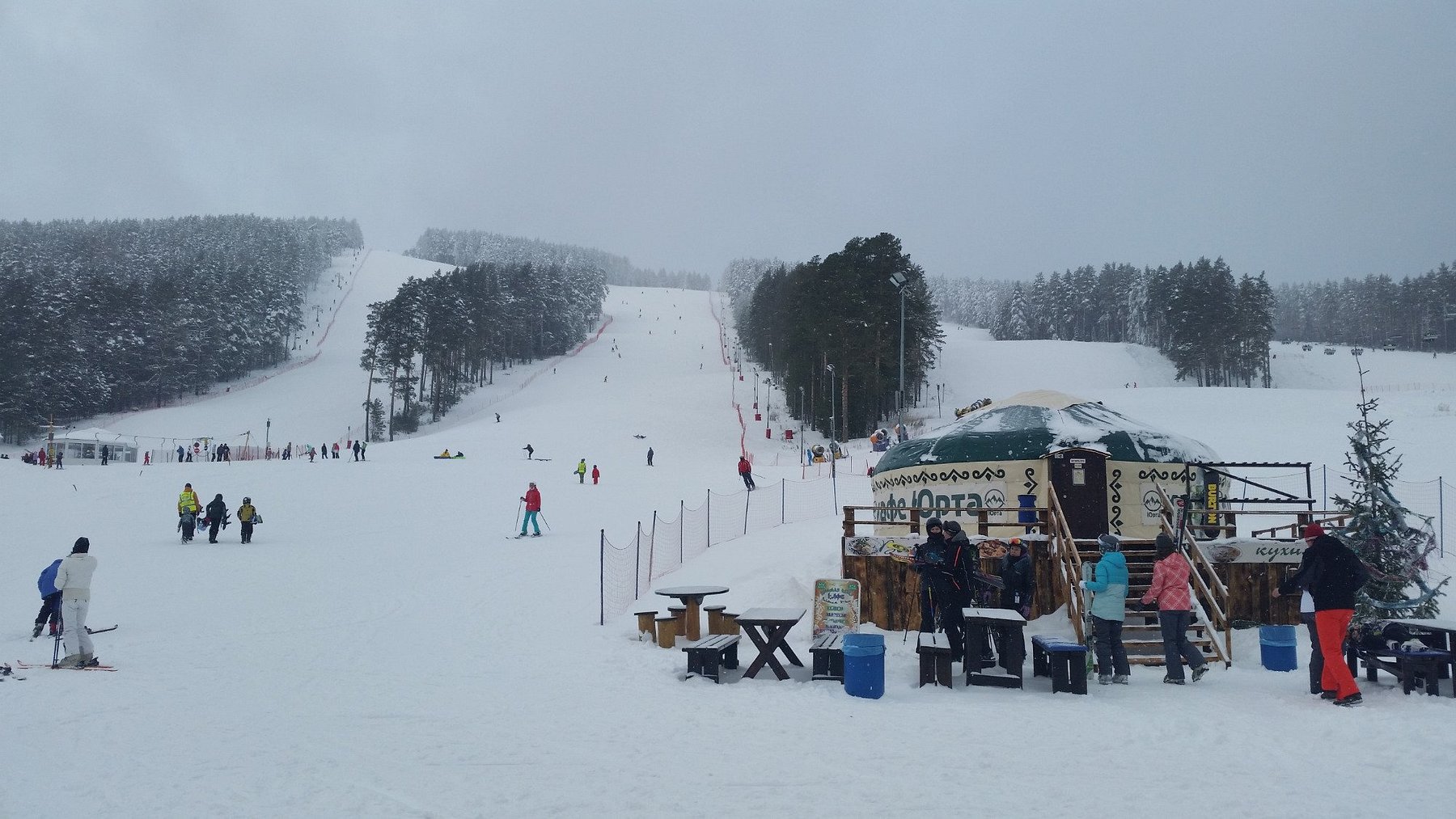 Winter sports scene at Mratkino in Beloretsk, Russia showcasing a busy ski resort, ski lift ferrying people, and snow-laden slopes amidst beautiful winter scenery.