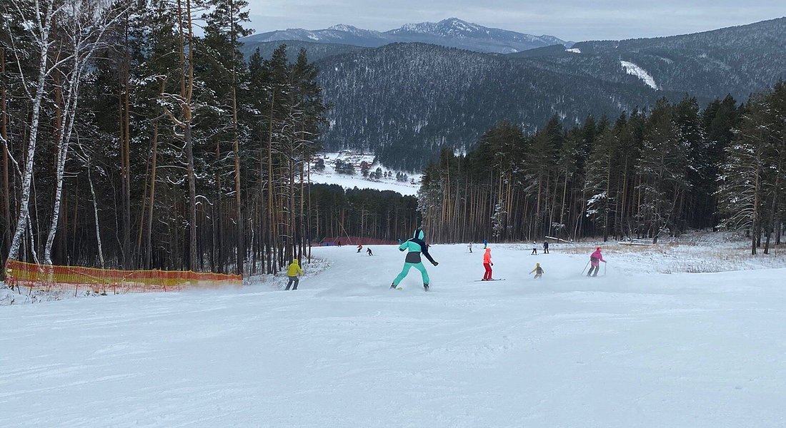 A dynamic winter sports scene at Mratkino in Beloretsk, Russia. A skier can be seen in action, surrounded by snow-clad peaks of the ski resort. Few families are also enjoying skiing in the background.