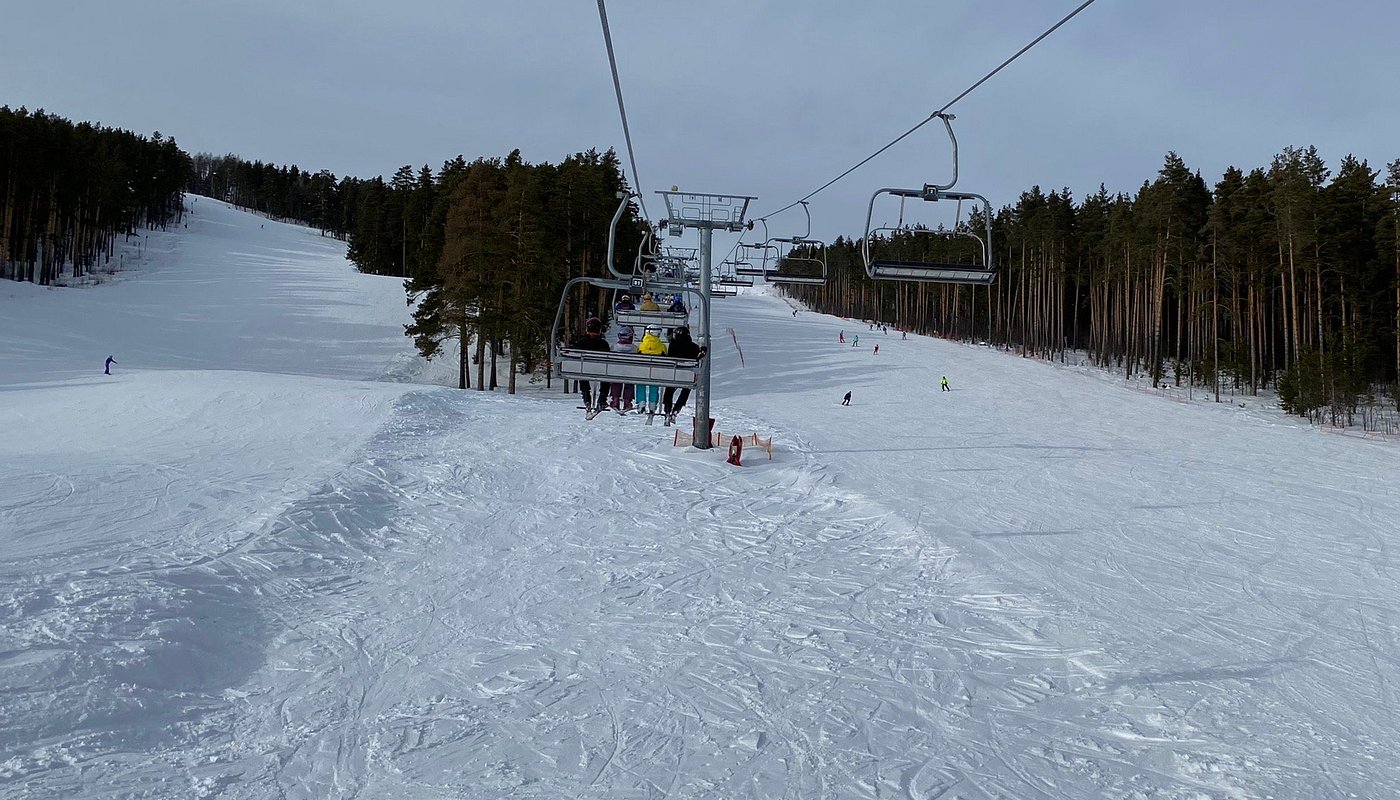 Ski lift ascends over snowy slopes at Mratkino ski resort in Beloretsk, Russia. Skiers take advantage of winter sports scene, chalet visible in the distance.