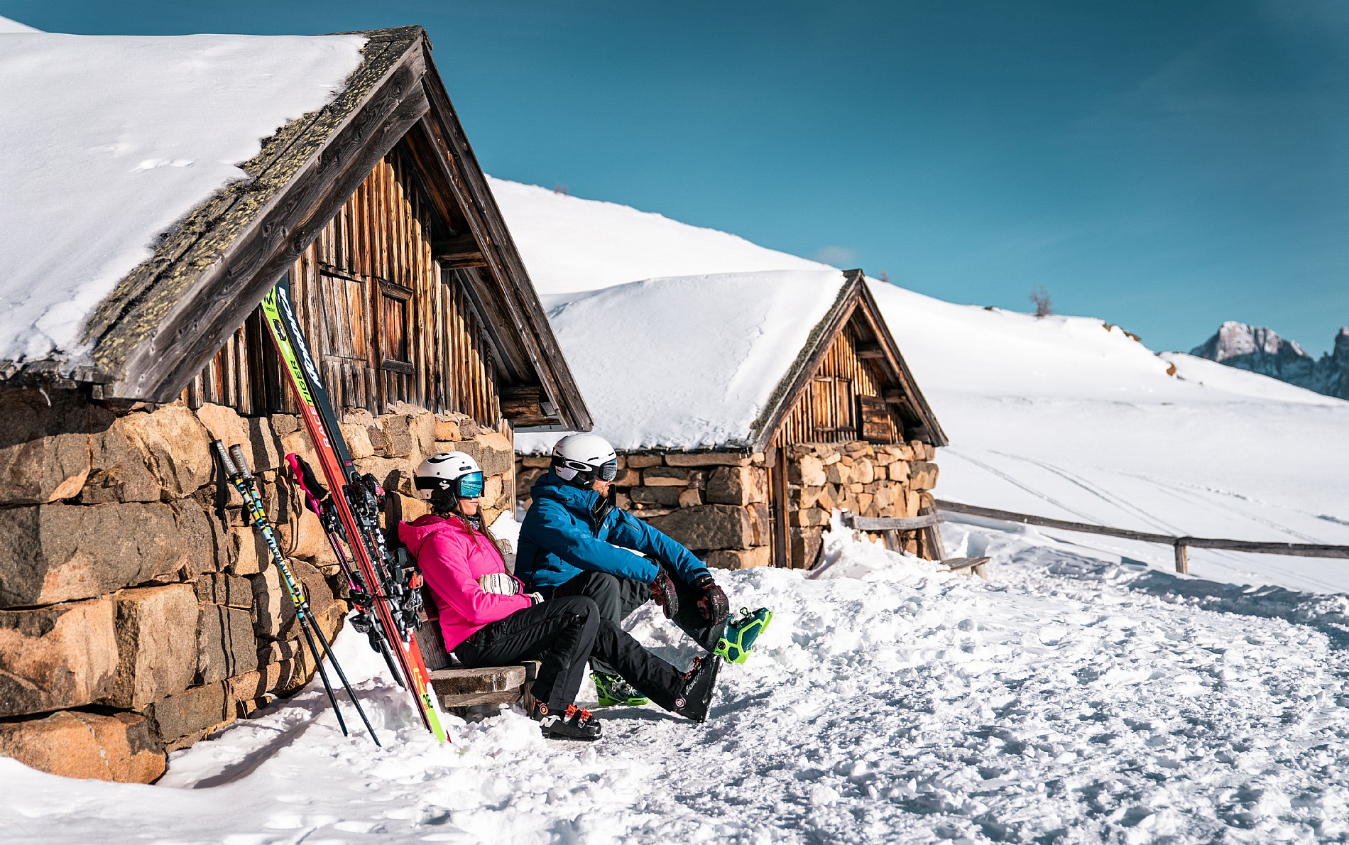 A family enjoying skiing at Alpe Lusia – Moena | Bellamonte ski resort in Trentino Italy with a quaint mountain hut in the backdrop of a bustling winter sports scene.