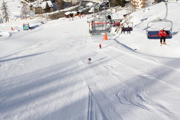 A picturesque winter scene at Valgrisenche ski resort in Italy featuring a quaint chalet skiers enjoying the snow and a ski lift ascending the mountain.