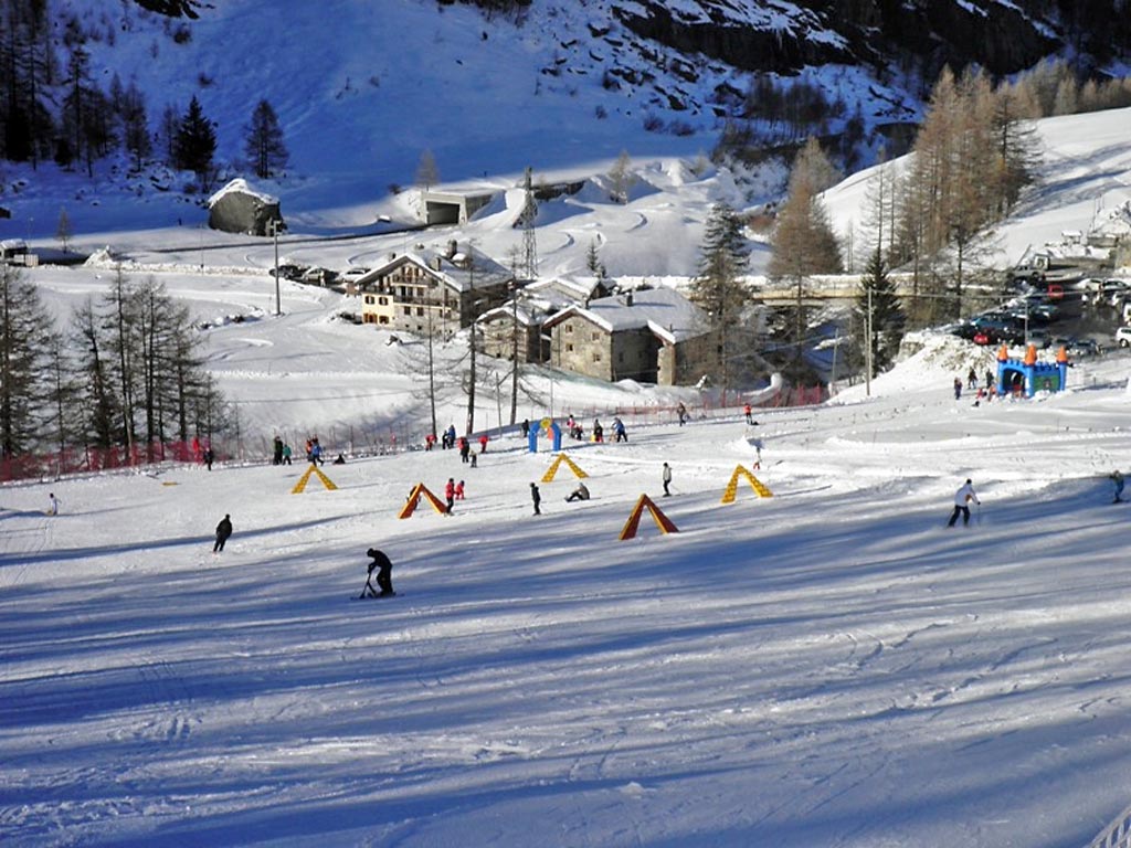Winter view of Valgrisenche in Gran Paradiso, Italy, featuring a bustling ski resort with a charming chalet amidst the snow-covered slopes and skiers enjoying the winter sports scene.