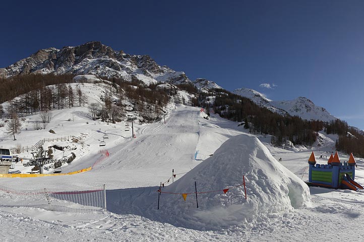 View of Valgrisenche in Italy showcasing a bustling winter sports center including a ski resort. A skier can be seen in action amidst a beautiful snowy landscape with a charming chalet in the backdrop.