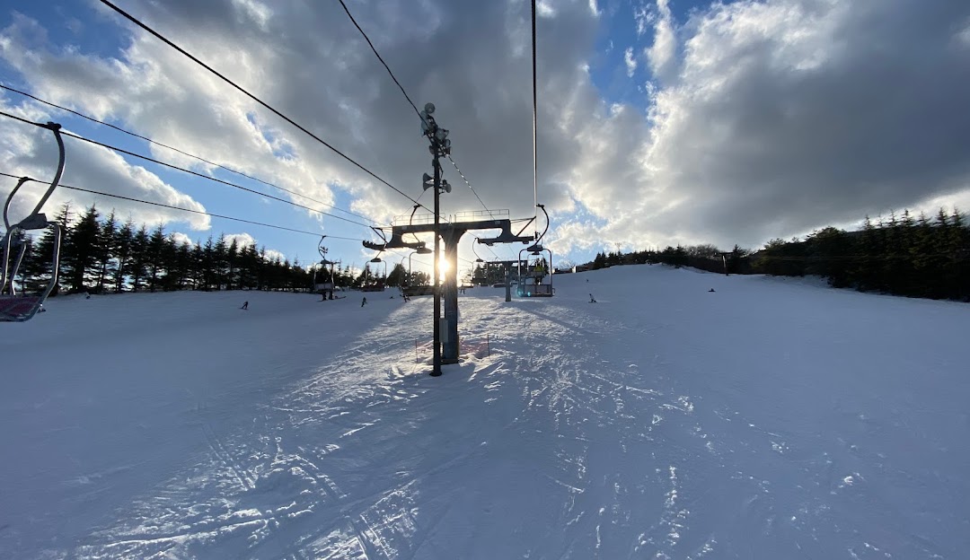 A winter scene at Osa Japan showcasing a ski lift in operation skiers gliding downhill a ski resort in view and a charming chalet nestled amongst the snow-clad peaks.