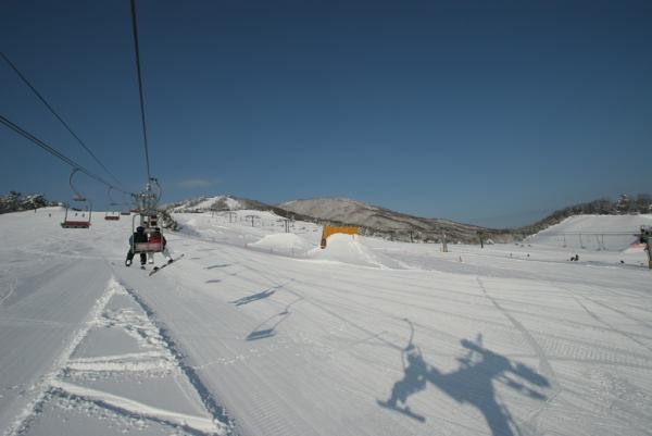 A winter scene from Osa Japan featuring a bustling ski resort. Ski lifts operate amongst snow-covered slopes while a charming challet stands nearby.