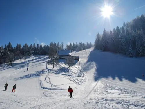 Winter scene at Ventron ski resort in Vosges, France featuring an snowy landscape with a skier on a trail and a ski lift in the background.