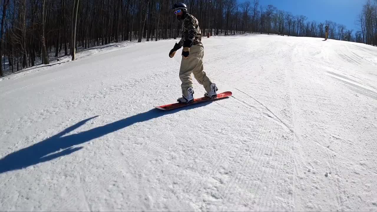 A snowboarder riding down the powdery slopes of Hatley Pointe in Mars Hill, North Carolina, with emerald evergreens around and a clear, crisp sky overhead. A picturesque winter landscape.