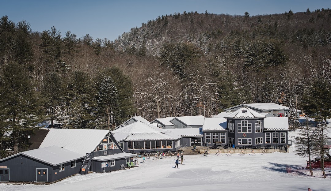Sundown ski resort in New Hartford, Connecticut during winter, with skiers enjoying the slopes under a beautiful sunset. The scene captures a bustling winter sports centre and lodge nestled amidst stunning winter scenery.