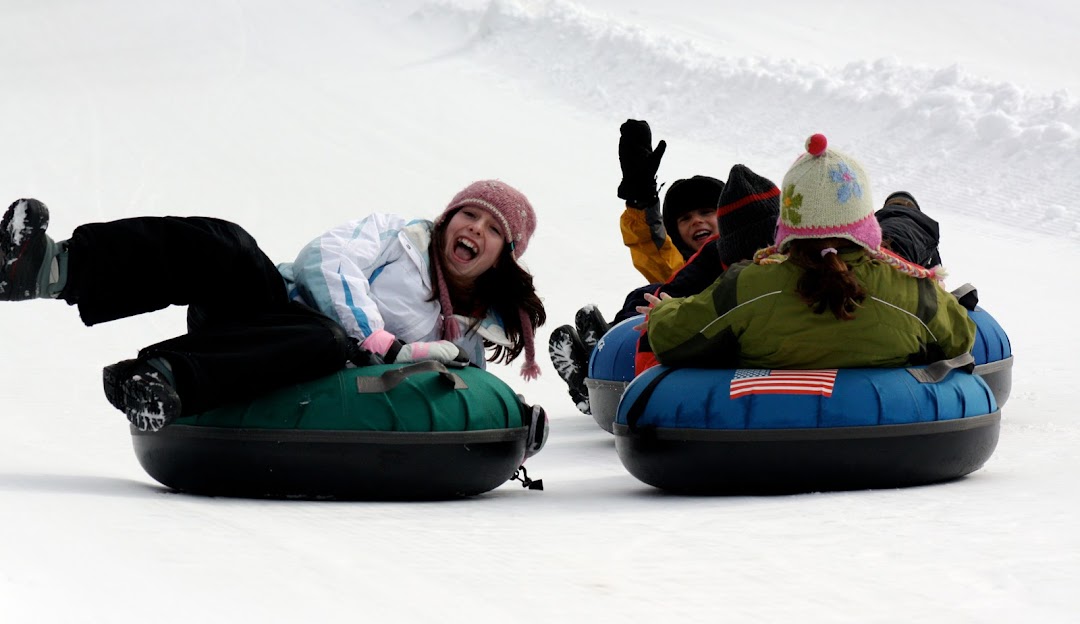 Winter sports enthusiasts in action at Granite Gorge Mountain Park, Roxbury, New Hampshire with a hint of a snowmobile and a ski lift in the backdrop of a ski resort.