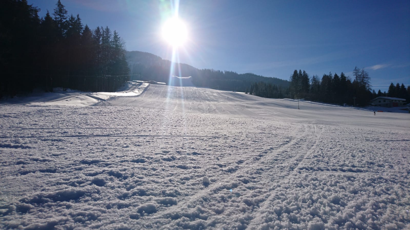 Winter sports scene at Schneeberglifte – Mitterland in Tyrol, Austria featuring a chalet on a sunny day, surrounded by snowy mountains and clear skies.