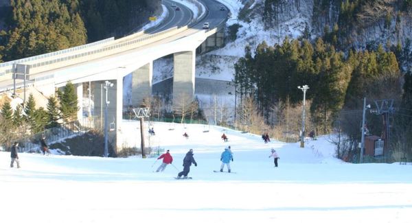 A winter sports scene at St Mary in Tōhoku, Japan, featuring an active winter sports centre amidst a snow-covered landscape with a chalet and ski resort in the background.