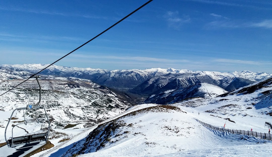 Overlooking a bustling winter scene at Leitariegos ski resort in Spain. A comfortable chalet sits in the foreground with a ski lift ascending nearby. Skiers dot the landscape enjoying the snowy slopes.
