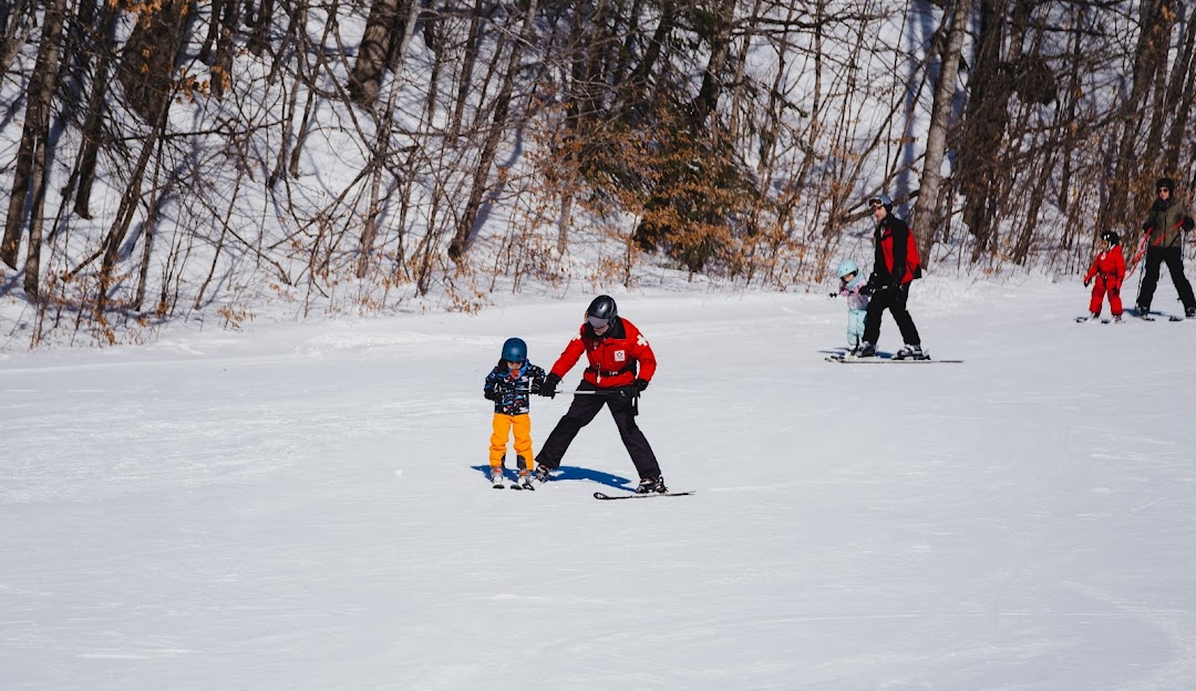 A family enjoying a day of winter sports at the Vorlage sports centre in Outaouais, Wakefield, Quebec, Canada, featuring a child learning to ski.