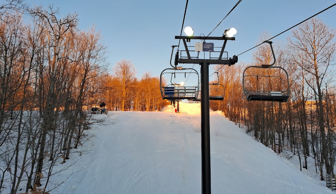 A scenic view of Crystal Mountain ski resort in Thompsonville Michigan featuring a ski lift against a wintery backdrop. Skiers can be spotted in the distance enjoying the snowy slopes.
