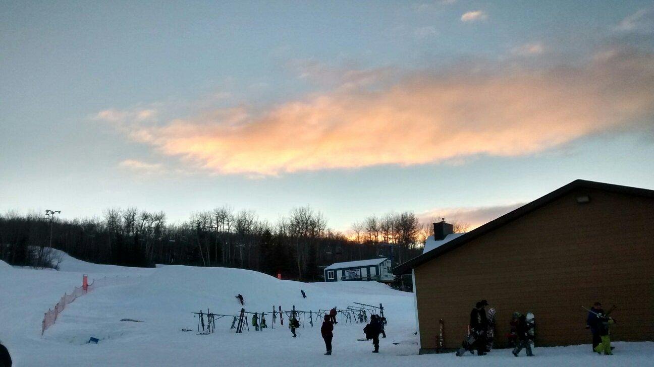 A bustling winter sports scene at Table Mountain in North Battleford, Saskatchewan, showcasing a ski resort with multiple skiers and a cozy chalet in the background.