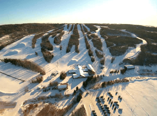 View of Table Mountain ski resort in North Battleford, Canada displaying a vibrant winter sports scene. Full of snow-covered slopes under a clear sky, the scene captures the essence of exhilarating winter sports.